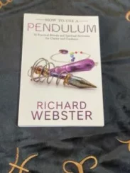 A photograph of a book titled 'How to use a Pendulum', by Richard Webster. The book cover features an intricate picture of a crystal pendulum, set against a white backdrop.